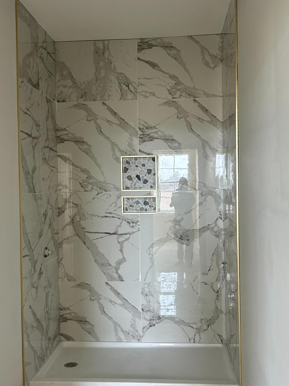 Marble-look tile shower with pebble niches